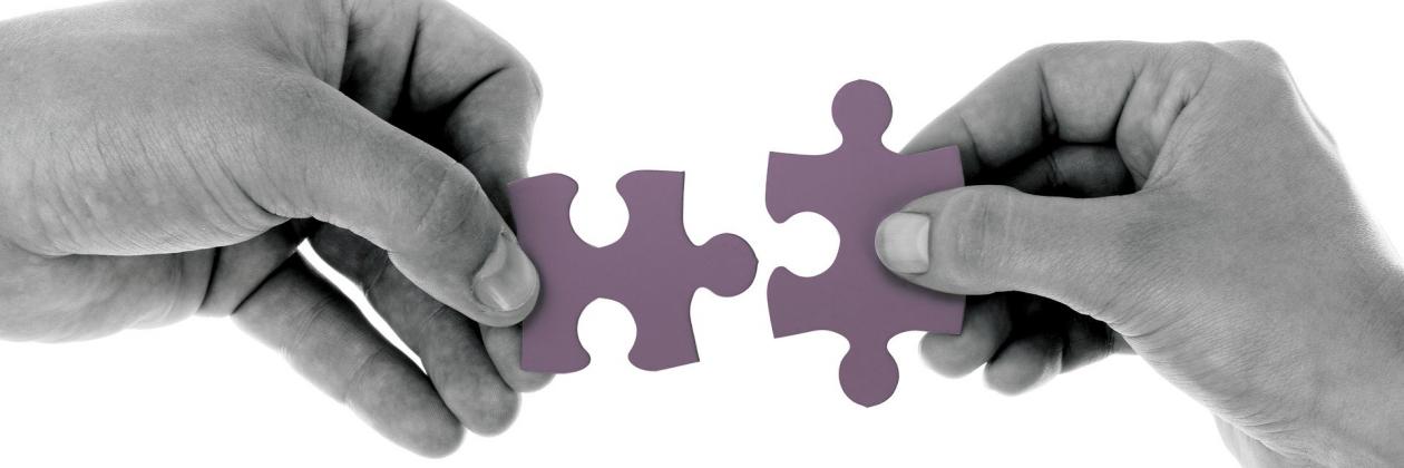 Two hands, each holding a jigsaw piece, reach towards each other