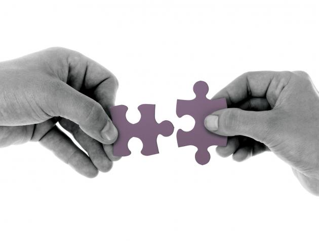 Two hands, each holding a jigsaw piece, reach towards each other